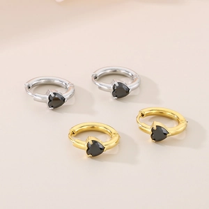 Close-up of heart-shaped gold and silver earrings with black stone inlay and snap closure