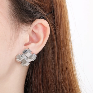 Gros plan d'une boucle d'oreille géométrique en acier inoxydable portée par un mannequin