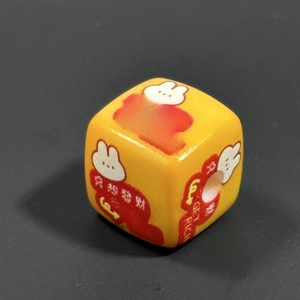 Macro shot of yellow acrylic keychain bead with Get Rich text and rabbit graphic