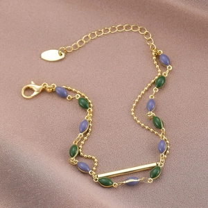 Dettaglio di un bracciale a doppio strato dorato con perline di smalto viola e verdi