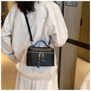 Detailed view of black textured leather bucket bag with silver zippers and top handle