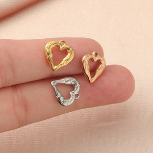 Three heart-shaped metal pendants in gold, rose gold, and silver on a finger for size