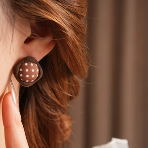 Close-up of brown fabric button earring with white polka dots worn on a model ear