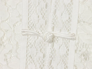 Close-up of white lace fabric detailing with intricate crochet patterns and button fastener