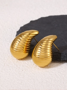 Macro detail of gold teardrop earrings with elegant spiral texture on stone surface