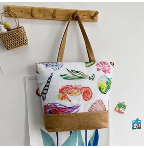 Close-up of canvas tote bag with watercolor sea horse and shell patterns hanging on wall