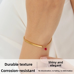 Close-up of golden link bracelet with curved plate and red heart pendant on wrist