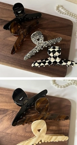 Close-up of four large acetate hair claws in various patterns on a dark wooden surface