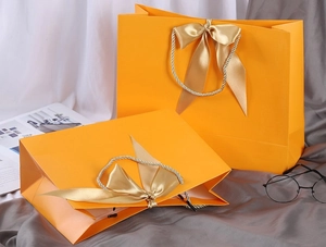 Detail view of orange gift bags with golden ribbon bows and textured matte finish