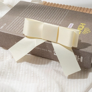 Detailed view of an elegant beige satin bow hair clip placed on a decorative book