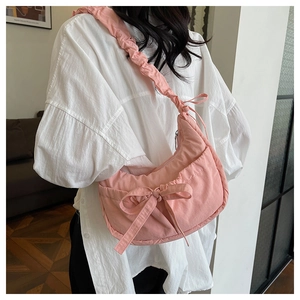 Pink pleated crossbody bag with bow decoration and ruffled strap shown on shoulder