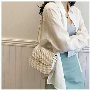 Detail of the woven straw bag with a gold horseshoe buckle and elegant leather strap