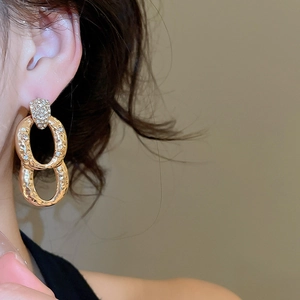 Close-up of golden double-ring earrings with zircon pavé and hammered metal texture