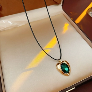 Detail of vintage heart necklace with green oval gemstone on a golden pendant
