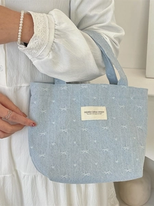 Sac à main en denim bleu clair avec nœuds blancs et écusson, porté avec une robe blanche