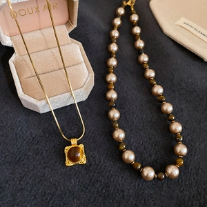 Detail of vintage tiger eye square pendant and champagne pearl necklace on grey fabric