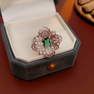 Macro shot of silver flower ring with green gemstone and crystals in a blue velvet box