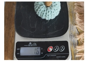 Detail shot of a handmade light green knitted pumpkin decoration on a scale weighing 16g