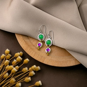 Detail of vintage feather earrings with green and purple gemstones on a wooden base