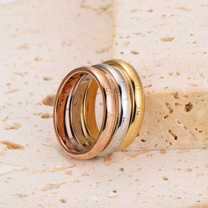 Set of four minimalist Roman numeral engraved stainless steel rings on a beige stone surface