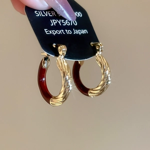 Macro shot of silver 925 earrings with gold rope texture and deep red enamel finish