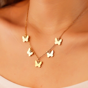 Detail of minimalist gold butterfly necklace with five pendants on a model's neck