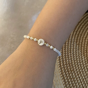 Detail of beaded shell bracelet with gold-tone letter P charm on a woman's wrist