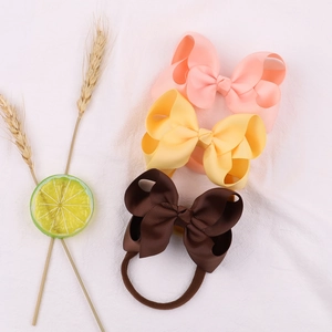 Three nylon baby headbands with ribbed ribbon bows in pink, yellow, and brown on white cloth