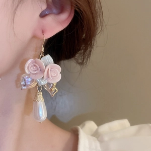 Close-up of pink rose flower earrings with water drop pearls on a model's ear