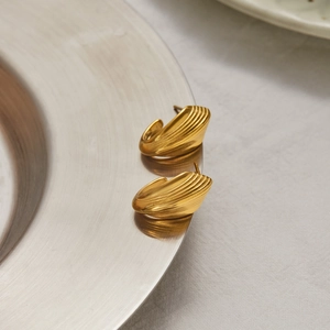 Dettaglio orecchini a conchiglia dorati con texture in metallo spazzolato su vassoio