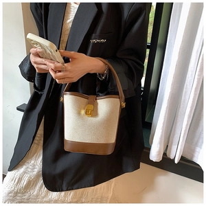 Detail of beige canvas and brown leather bucket bag with gold lock held by a model