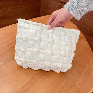 Detail of white quilted puffy cloud makeup bag with gold zipper and checkered texture