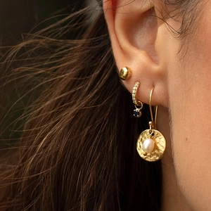Close-up of golden hammered earrings with blue gemstone and pearl drops on a model