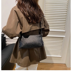 Détail d'un sac bandoulière en cuir tressé noir porté avec un trench-coat marron