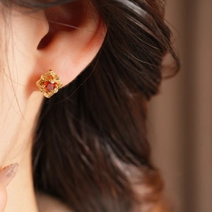 Close-up of golden floral stud earring with a red gemstone on earlobe