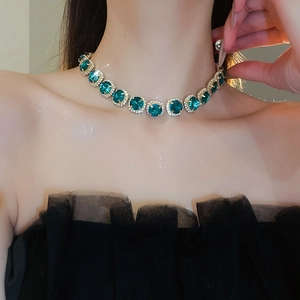 Close-up of elegant emerald green square pendant necklace with diamond halo on model