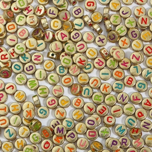 Dettaglio di perline dorate con lettere colorate per la creazione di gioielli fai-da-te