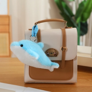 Close-up of a blue plush dolphin keychain hanging on a stylish handbag accessory