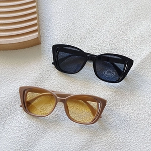 Detail showing UV400 lenses on black and khaki cat-eye sunglasses for kids on white surface