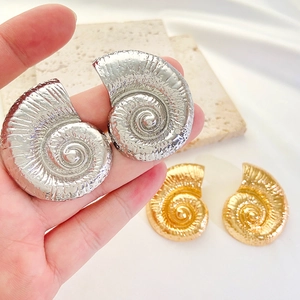 Macro detail of spiral conch shell earrings in polished gold and silver metal finishes