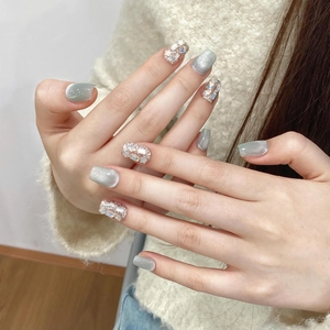 Detail of grey cat-eye press-on nails with sparkling rhinestones on soft white knit