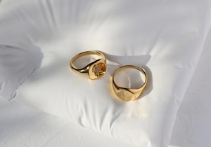 Detail view of 18K gold-plated butterfly and flower signet rings on a soft white cushion