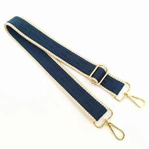 Detail of adjustable blue and beige woven bag strap with golden metal swivel hooks