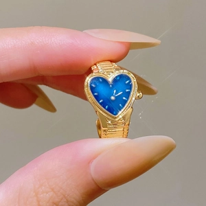 Detailed view of a mini heart-shaped gold watch ring with a deep blue dial on finger