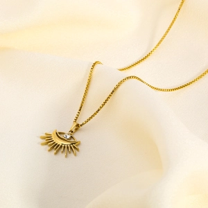 Macro view of gold evil eye sun pendant with zircon on a soft beige silk background