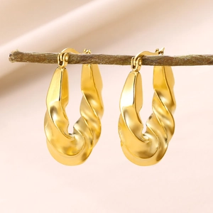 Close-up of golden geometric twisted earrings hanging on a thin wooden branch branch