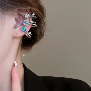 Détail de trois bagues d'oreille en cristal coloré portées pour un look Y2K tendance