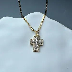 Detailed macro view of a gold cross pendant necklace featuring shimmering clear zircon stones