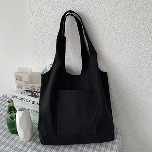 Detailed view of black canvas tote bag with large front pocket against a white wall