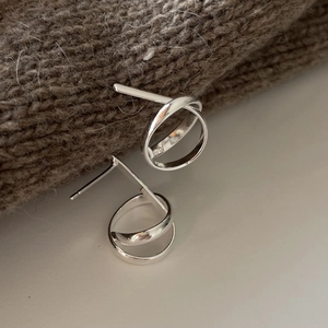 Macro shot of silver knot stud earrings displayed on brown knit fabric texture